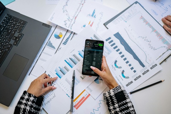 Hands comparing printed price charts with a smartphone