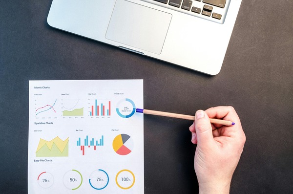 Hand pointing at printed charts beside a laptop