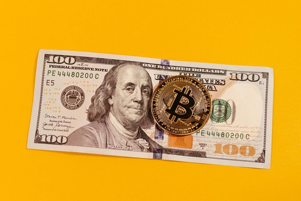 Bitcoin coin resting on a US dollar banknote on a yellow background